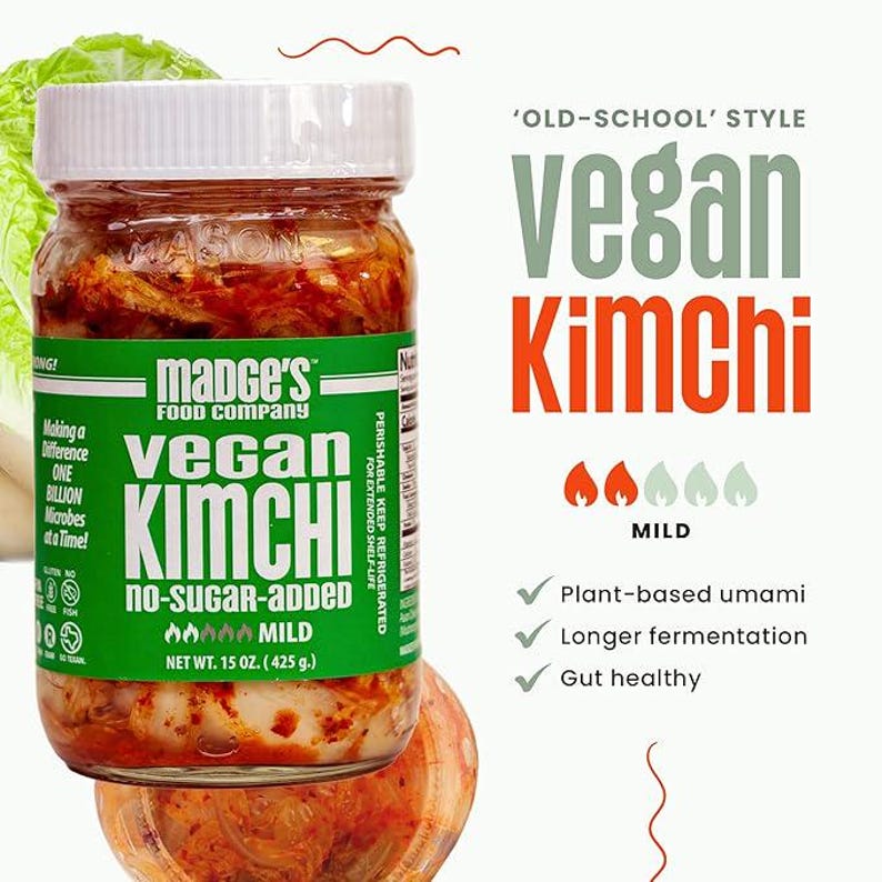 May include: A jar of vegan kimchi from Madge's Food Company. The jar has a white lid and a green label with the words "vegan kimchi" in large letters. The label also states "no-sugar-added" and "mild". The jar contains 425 g. of kimchi.