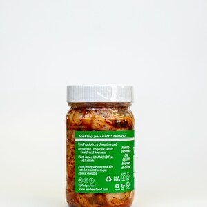 May include: A glass jar with a white lid, filled with a reddish-orange fermented food product. The jar has a green label with text including "Making you GUT STRONG!" and "Live Probiotics & Unpasteurized". The product is plant-based and contains no fish or shellfish.