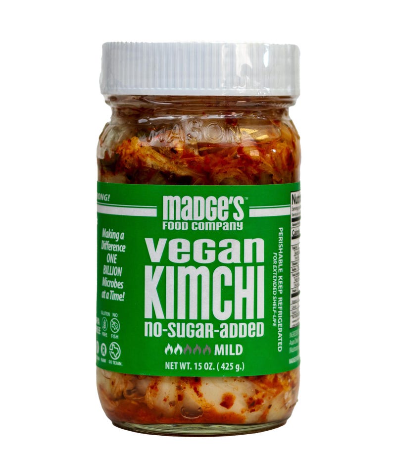 May include: A glass jar of Madge's Vegan Kimchi with a white lid. The jar has a green label with the words "Vegan Kimchi" and "No-Sugar-Added." The net weight is 425 g. The kimchi appears to be a mild variety.