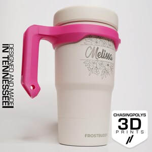 May include: A white insulated tumbler with a pink handle and lid. The tumbler has the name "Melissa" engraved with floral accents. The text "Designed and Made in Tennessee" is on the left side. The logo "Chasingpolys 3D Prints" is on the right.