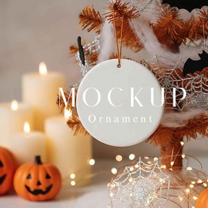 Könnte beinhalten: Ein weißer, runder Ornament mit den Wörtern „MOCKUP“ und „Ornament“ aufgedruckt. Der Ornament hängt an einem kleinen orangefarbenen Faden. Der Hintergrund umfasst einen kleinen orangefarbenen Baum, der mit Spinnweben, Fledermäusen und Kürbissen dekoriert ist.