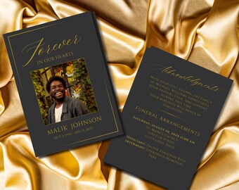 May include: Two black memorial cards with gold accents rest on a gold satin surface. The front card reads "Forever in Our Hearts" above a photo of Malik Johnson. The second card lists funeral arrangements.