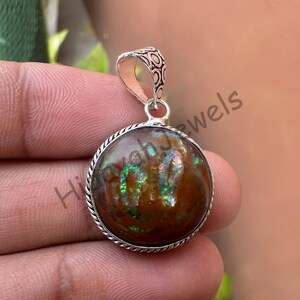 May include: A round pendant with a brown, iridescent stone set in a silver-colored metal frame. The pendant has a decorative bail and a textured border. The stone displays green and gold hues.