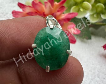 May include: A green oval gemstone pendant with a silver bail and accents. The pendant is held up by a person's fingers. The text "Hidayah Jewels" is written on the pendant.