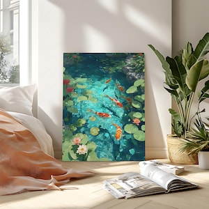 May include: A framed art print depicts a serene koi pond scene. The artwork showcases vibrant orange and white koi fish swimming in turquoise water, surrounded by lily pads and pink lotus flowers. The painting is displayed in a bright room with natural light.