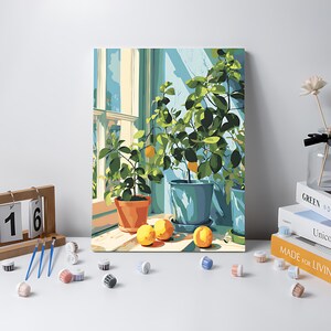 May include: A painting of potted lemon trees in front of a window. The painting features green leaves, yellow lemons, and blue-green pots. The painting is on a white surface with paint supplies and books.