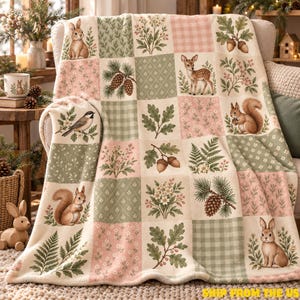 May include: A soft throw blanket featuring a patchwork design of woodland animals including rabbits, a deer, and a squirrel, interspersed with botanical illustrations of pinecones, acorns, ferns, and flowers in shades of sage green, pink, and cream.