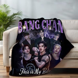 May include: A black plush blanket with a group of people and the text "BANG CHAN" in purple and "This is My Bar" in white. The blanket has a dark background with lightning bolt graphics.