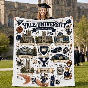 May include: A white blanket with a detailed design featuring "YALE UNIVERSITY" and university landmarks. The design includes baseballs, a baseball bat, and a cat wearing a Yale jersey. The blanket is held by a person in a graduation cap.