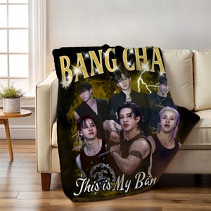 May include: Black throw blanket with a gold "BANG CHAN" text and a group of six people. The blanket also has the text "This is My Ban" in white script. The background features a yellow lightning bolt design.