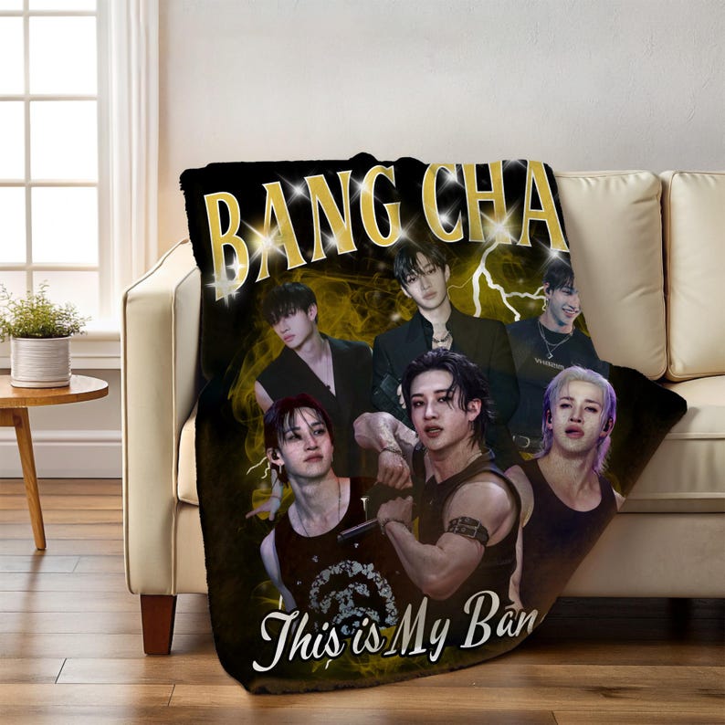 May include: Black throw blanket with a gold "BANG CHAN" text and a group of six people. The blanket also has the text "This is My Ban" in white script. The background features a yellow lightning bolt design.