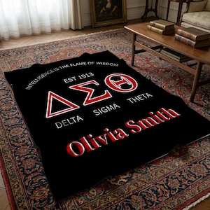 Puede incluir: Una manta rectangular negra con las letras griegas Delta Sigma Theta en rojo y blanco, el texto EST 1913, la frase INTELLIGENCE IS THE FLAME OF WISDOM y el nombre Olivia Smith impreso en una fuente roja y blanca en negrita.