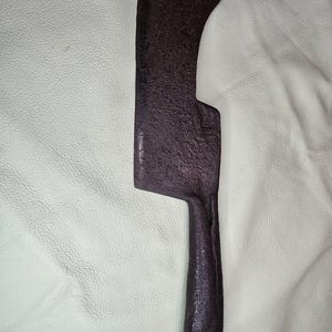 May include: A dark brown cleaver with a curved blade and a textured handle. The cleaver has a hole near the top of the blade. The cleaver is made of metal and shows signs of use.