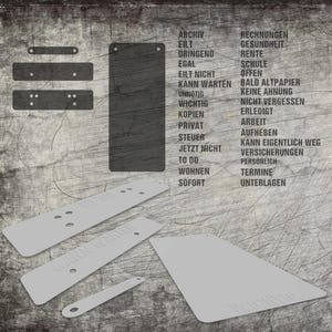 Op de afbeelding: Een set donkergrijze rechthoekige labels met afgeronde hoeken en voorgeboorde gaten. De labels bevatten een lijst met Duitse woorden, waaronder ARCHIV, EILT, DRINGEND, EGAL, EILT NICHT, KANN WARTEN, UNNÖTIG, WICHTIG, KOPIEN, PRIVAT, STEUER, JETZT NICHT, TO DO, WOHNEN, SOFORT, RECHNUNGEN, GESUNDHEIT, RENTE, SCHULE, OFFEN, BALD ALTPAPIER, KEINE AHNUNG, NICHT VERGESSEN, ERLEDIGT, ARBEIT, AUFHEBEN, KANN EIGENTLICH WEG, VERSICHERUNGEN, PERSÖNLICH, TERMINE en UNTERLAGEN.