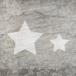 Peut inclure: Deux décorations en forme d'étoile blanche avec un design superposé, sur un fond gris texturé. Les étoiles varient en taille, avec une plus petite à droite d'une plus grande. Chaque étoile a un petit trou en haut pour l'accrochage.
