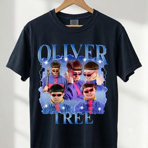 May include: A black short-sleeve t-shirt featuring a graphic print of Oliver Tree. The design includes multiple images of the artist wearing a bowl cut and red sunglasses, set against a blue lightning background with the text OLIVER TREE.