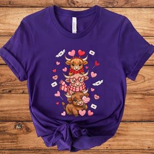 May include: A purple t-shirt featuring a stacked design of three cartoon Highland cows. The cows are adorned with heart-shaped balloons, scarves, and glasses, with hearts and love letters scattered around. The shirt is made of soft material.