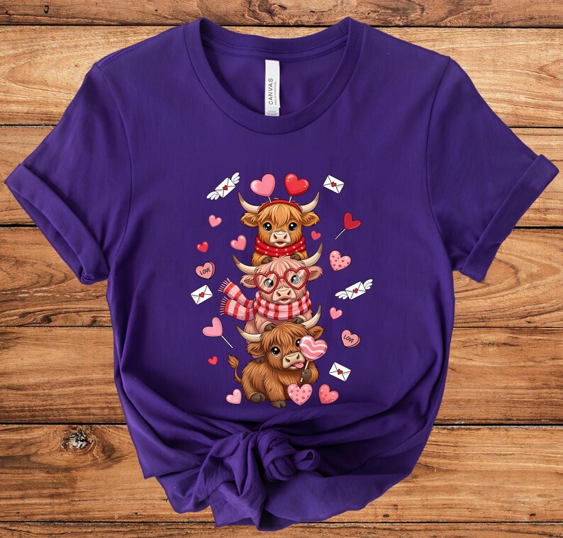 May include: A purple t-shirt featuring a stacked design of three cartoon Highland cows. The cows are adorned with heart-shaped balloons, scarves, and glasses, with hearts and love letters scattered around. The shirt is made of soft material.