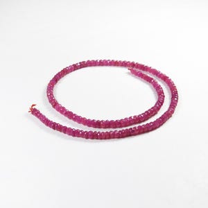 May include: A strand of faceted, deep pink ruby beads. The beads are strung together, forming a continuous loop. The ruby beads are small and uniform in size, with a polished, reflective surface. The background is plain white.