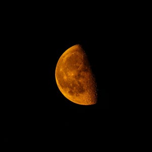 Peut inclure: Gros plan d'un croissant de lune dans le ciel nocturne. La lune est d'une couleur orange vif, avec une surface texturée. Le fond est complètement noir, créant un contraste saisissant avec la lune.