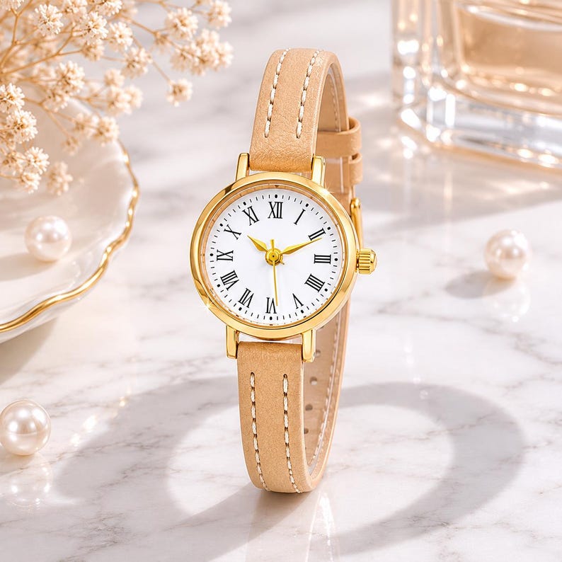 May include: A gold-toned wristwatch with a white face and Roman numeral hour markers. The watch has a light brown leather band and gold hands. The watch face is approximately 1 inch in diameter.