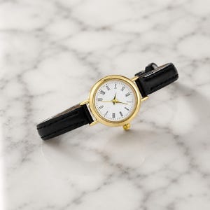 May include: A gold-tone wristwatch with a white face and black leather band. The watch features Roman numeral hour markers and gold hands. The band is approximately 0.5 inches wide. The watch is displayed on a marble surface.