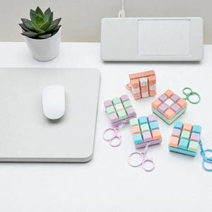 May include: A collection of colorful, pastel-colored keyboard keycap cube keychains. The keychains are in various colors, including pink, orange, green, blue, and purple. A white mouse and a small potted succulent are also visible.