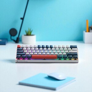 May include: A compact mechanical keyboard with a white and grey keycap layout, accented by a red space bar. The keyboard features multi-coloured LED backlighting and the text "MACHENIKE K500 MECHANICAL KEYBOARD". A blue notepad and a white mouse are in the foreground.