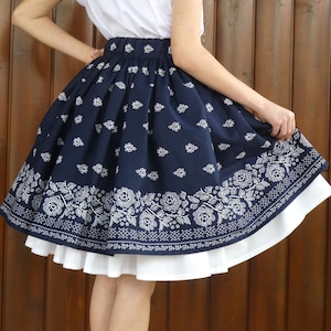 Può includere: Gonna blu navy con motivo floreale bianco e sottogonna bianca. La gonna presenta un bordo floreale dettagliato e una vita arricciata. Lo stile è femminile e classico, adatto a varie occasioni.