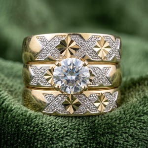 May include: A three-piece gold ring set featuring a central round brilliant-cut clear stone. Each band displays a repeating pattern of polished gold star-shaped motifs alternating with textured, granular sections and X-shaped engravings.