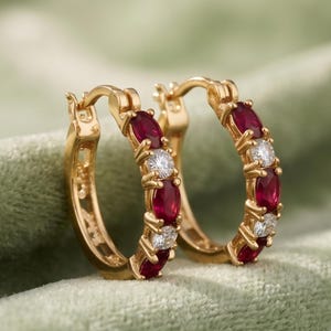 Könnte beinhalten: Ein Paar goldene Creolen mit einem abwechselnden Muster aus oval geschliffenen, tiefroten Rubinen und rund geschliffenen, klaren weißen Diamanten. Die Steine sind in einer Krappenfassung entlang der Vorderseite jedes Reifens angebracht.