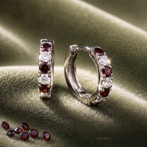 May include: A pair of hoop earrings crafted from 14k gold, featuring an alternating pattern of round-cut deep red garnet gemstones and clear white diamonds. The earrings have a hinged closure mechanism and are displayed with loose red stones.