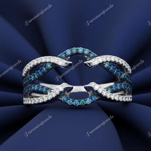 May include: A silver ring with a double band design. The ring features a row of small, round, blue gemstones and a row of white gemstones. The ring is set against a dark blue background.