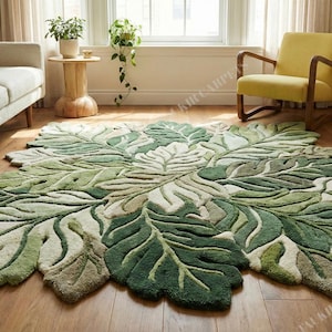 Puede incluir: Una alfombra grande con forma de hoja en tonos verdes y crema, que se asemeja a una planta gigante. La alfombra está colocada sobre un suelo de madera en un salón, con un sofá y una silla visibles en el fondo. El diseño de la alfombra añade un elemento natural a la habitación.