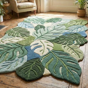 May include: A large, leaf-shaped rug in shades of green, blue, and cream. The rug features a detailed monstera leaf design, adding a touch of nature to the room. The rug is placed on a wooden floor.