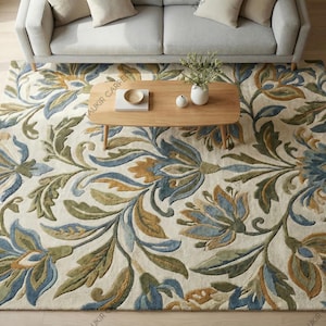 May include: A large rectangular area rug with a floral pattern in shades of blue, green, and gold on a cream background. The rug is placed under a light gray sofa and a wooden coffee table.