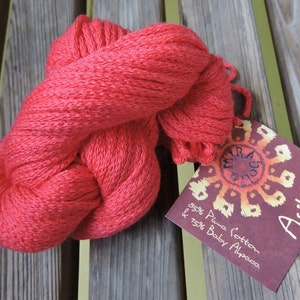 Könnte beinhalten: Ein Knäuel roter Wolle mit dem Etikett "Ashikuta" und dem Text "85% Pima Cotton & 15% Baby Alpaca".