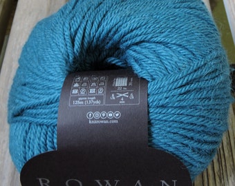 May include: Teal blue yarn ball with a black label that says "Rowan" and includes care instructions and yarn information. The label also says "125m (137yds)" and "knitrowan.com".