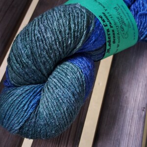 K&ouml;nnte beinhalten: Eine Kn&auml;uel blaues und gr&uuml;nes Garn mit dem Etikett "Modern Era Ocean Realm" Wolle/Acryl 113 yds.