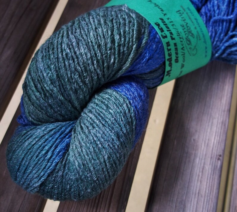 K&ouml;nnte beinhalten: Eine Kn&auml;uel blaues und gr&uuml;nes Garn mit dem Etikett "Modern Era Ocean Realm" Wolle/Acryl 113 yds.