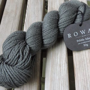 Könnte beinhalten: Ein Knäuel dunkelgraues Garn mit der Aufschrift "Rowan Pebble Island", hergestellt aus Shetlandwolle. Das Etikett zeigt auch "50g".