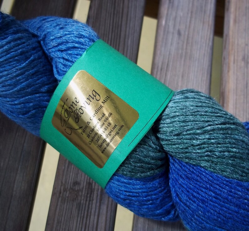 K&ouml;nnte beinhalten: Blau-gr&uuml;nes Garnkn&auml;uel mit einem Etikett mit der Aufschrift "Done Moving Farm & Carding Mill 20 Charlotte Road Charlotte, Maine 04666 207-454-8148 Farrarps@gwi.net www.deneroving.com"