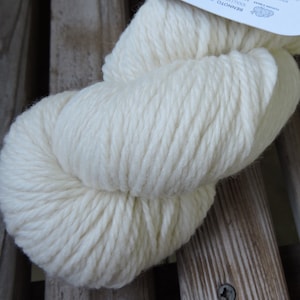 May include: A skein of white yarn, made of wool, is shown on a wooden surface. The yarn is soft and fluffy, and it is perfect for knitting or crocheting.