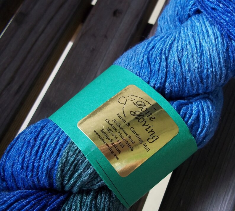 K&ouml;nnte beinhalten: Eine blaue Garnrolle mit einem gr&uuml;nen Etikett, auf dem "Done Roving Farm & Carding Mill" mit Kontaktinformationen steht.
