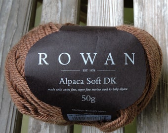 May include: A brown ball of Rowan Alpaca Soft DK yarn, a blend of 70% virgin wool and 30% alpaca, with a label that reads "ROWAN EST 1978 Alpaca Soft DK made with extra fine, super fine merino wool & baby alpaca 50g Sh:00203".
