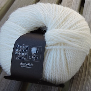 May include: A ball of white yarn with a brown label that includes care instructions, yarn weight, and length. The label reads "approx length 125m (137yds)", "10cm/4in 22 sts", "9 UK 3 1/2 US", and "knitrowan.com".