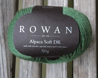 May include: A ball of green Rowan Alpaca Soft DK yarn with a black label that reads "ROWAN EST 1978 Alpaca Soft DK made with extra fine, super fine merino wool & baby alpaca 50g".
