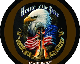 May include: Circular design with a bald eagle, American flag, and military boots. Text reads "Home of the Free Because of the Brave" and "Lest We Forget". The design is set against a black and brown background.