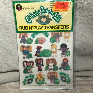 May include: Sealed package of Cabbage Patch Kids Rub N' Play Transfers. The package features a green and yellow header with the Cabbage Patch Kids logo and the words "RUB N' PLAY TRANSFERS". The sheet contains various Cabbage Patch Kids characters in different poses.