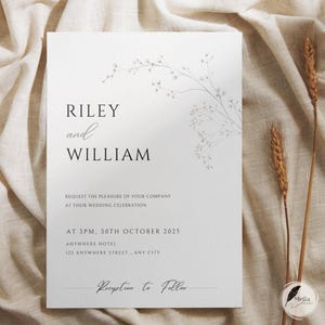 Pode incluir: Um convite de casamento branco com os nomes "RILEY and WILLIAM" em texto preto. O convite inclui o texto "REQUEST THE PLEASURE OF YOUR COMPANY AT THEIR WEDDING CELEBRATION" e detalhes do evento. Um design floral está no canto superior direito.